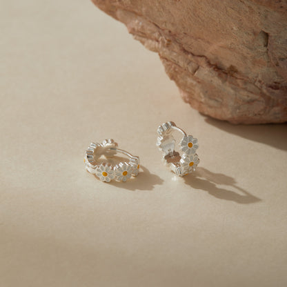 Elegant sterling silver enamel daisy hoop earrings photographed in soft natural light.