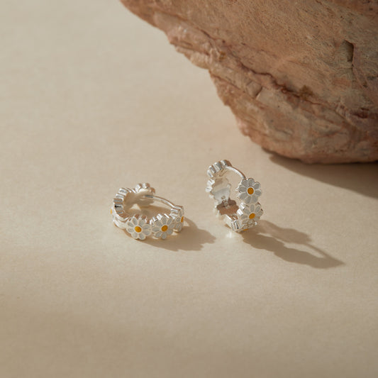 Elegant sterling silver enamel daisy hoop earrings photographed in soft natural light.