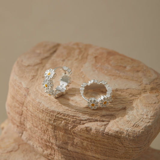 Handcrafted sterling silver daisy hoop earrings styled on textured stone surface.