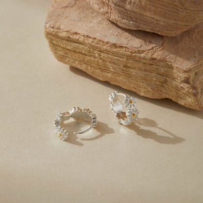 Close-up of sterling silver daisy hoop earrings with enamel flowers on neutral background.