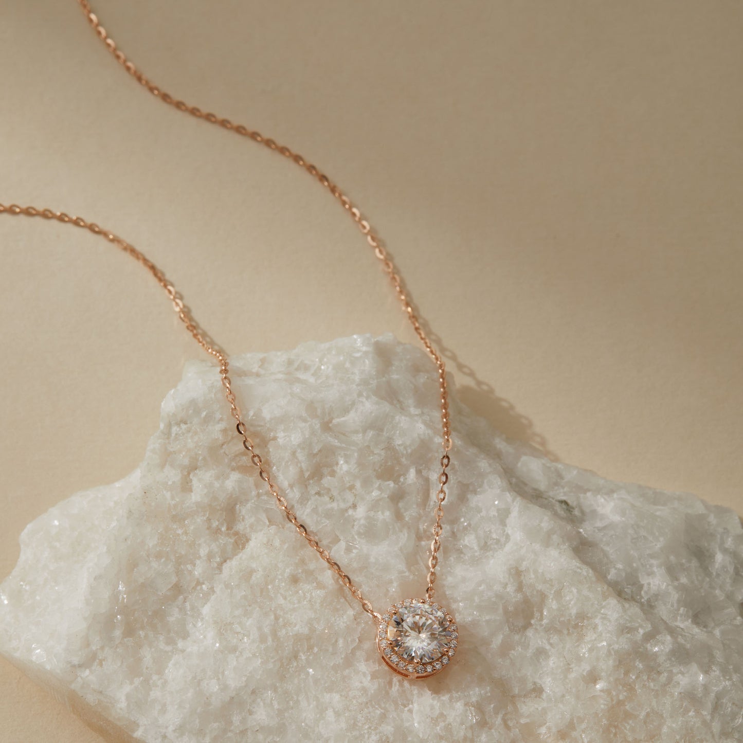 Rose gold-plated moissanite halo pendant necklace full chain view on white quartz