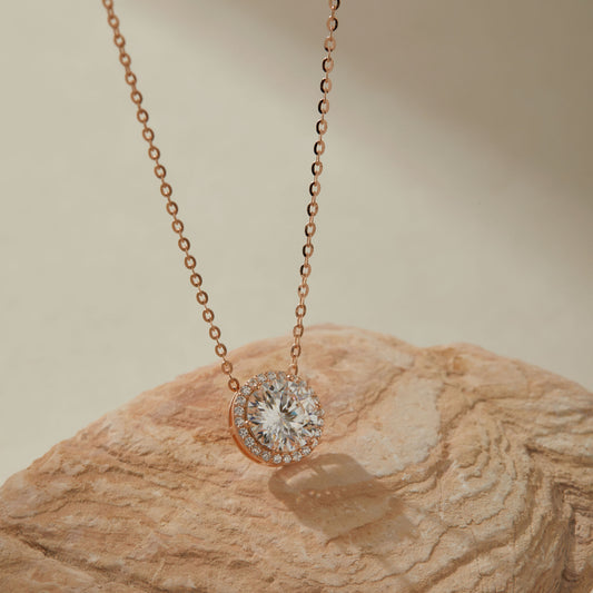 Rose gold-plated 2ct moissanite round halo pendant necklace on sandstone, close-up of pendant
