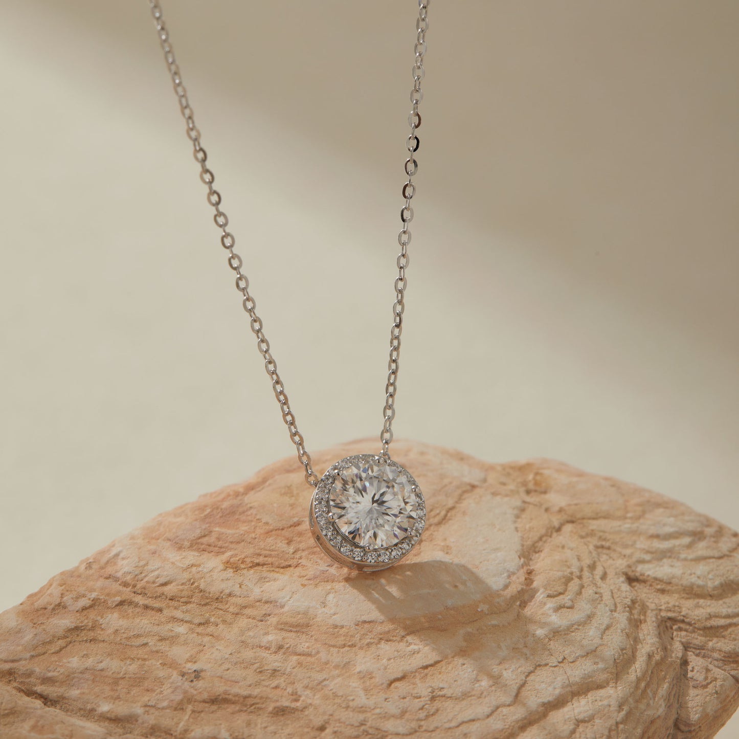 White gold-plated 2ct moissanite round halo pendant necklace on sandstone, close-up