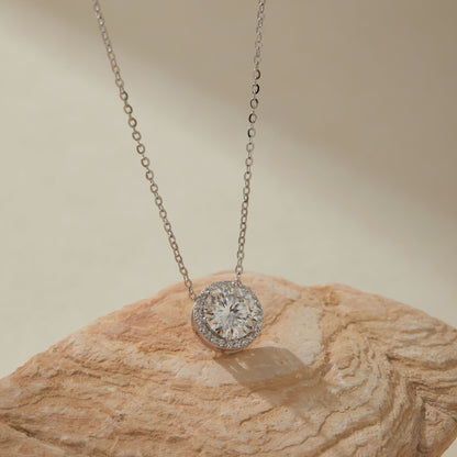 White gold-plated 2ct moissanite round halo pendant necklace on sandstone, close-up