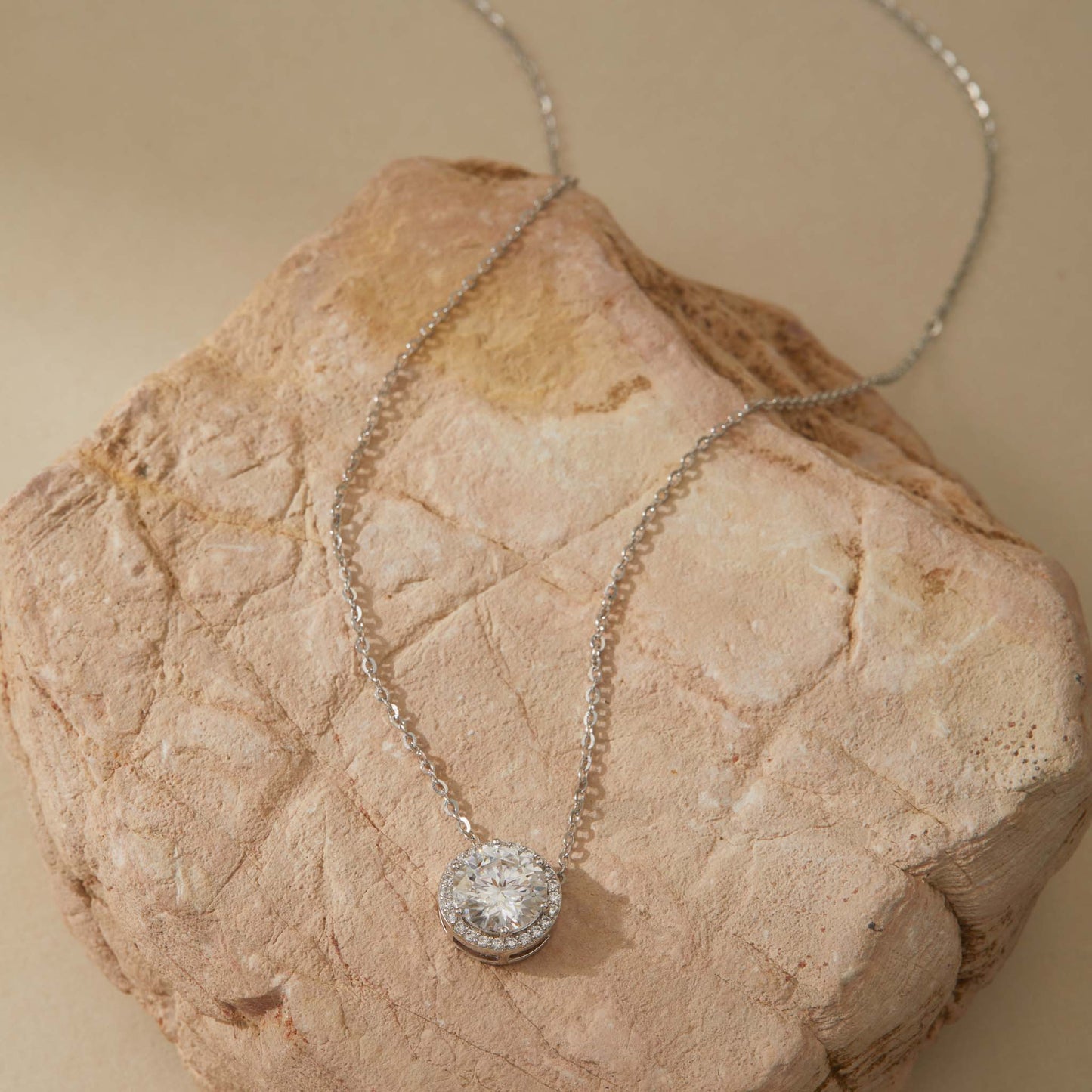 White gold-plated moissanite halo pendant necklace full chain view on sandstone
