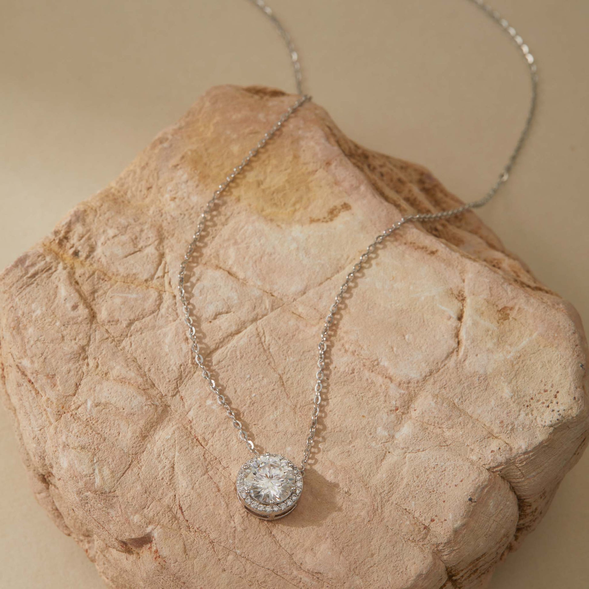 White gold-plated moissanite halo pendant necklace full chain view on sandstone