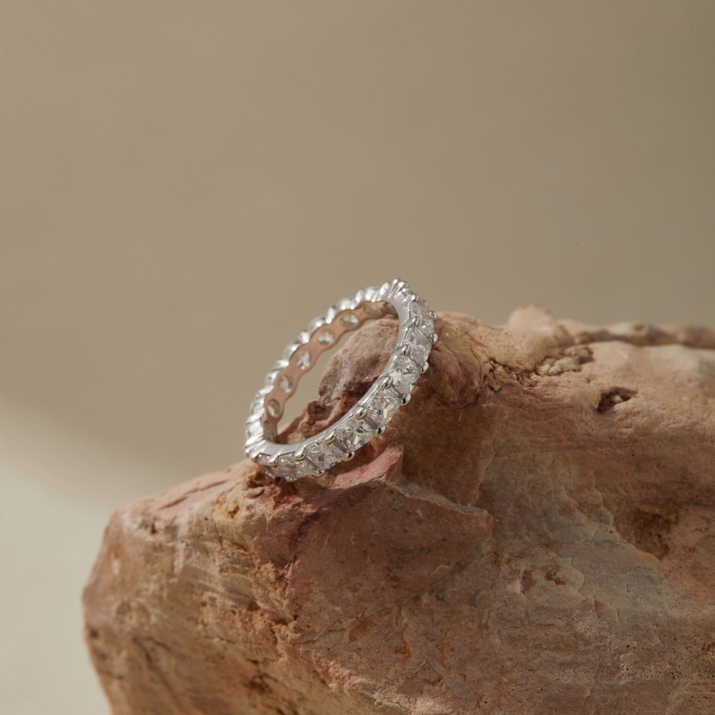 Round and princess-cut silver eternity ring styled on a neutral background