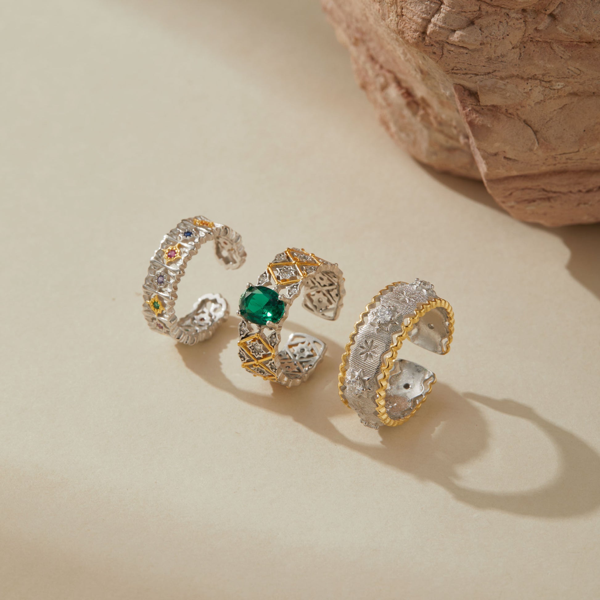 Three sterling silver adjustable rings with crystal accents — floral multicolor ring, emerald green gemstone ring with gold accents, and silver starburst ring with gold edge