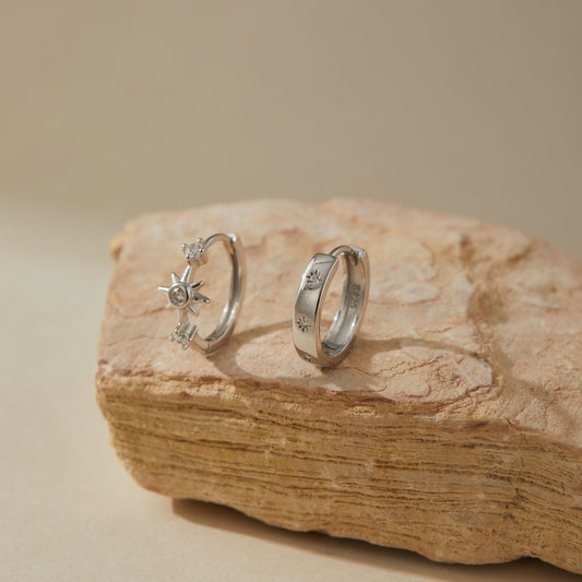 Close-up of asymmetric starburst huggie earrings on textured stone surface
