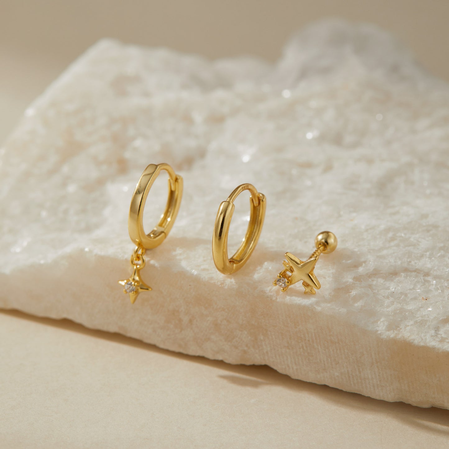 Three gold plated star earrings on white quartz, plain huggie, star drop huggie and stud