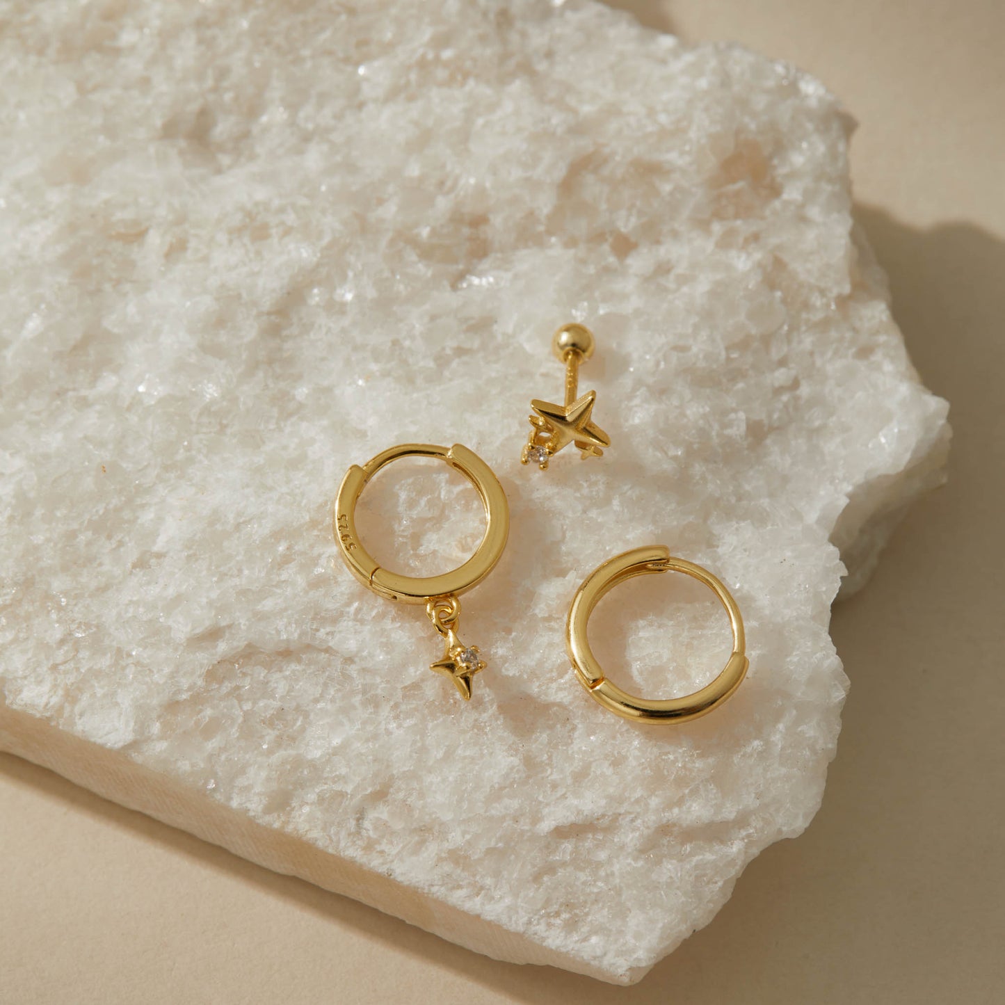 Overhead view of the gold star earring set on white quartz, 925 stamp visible on a huggie