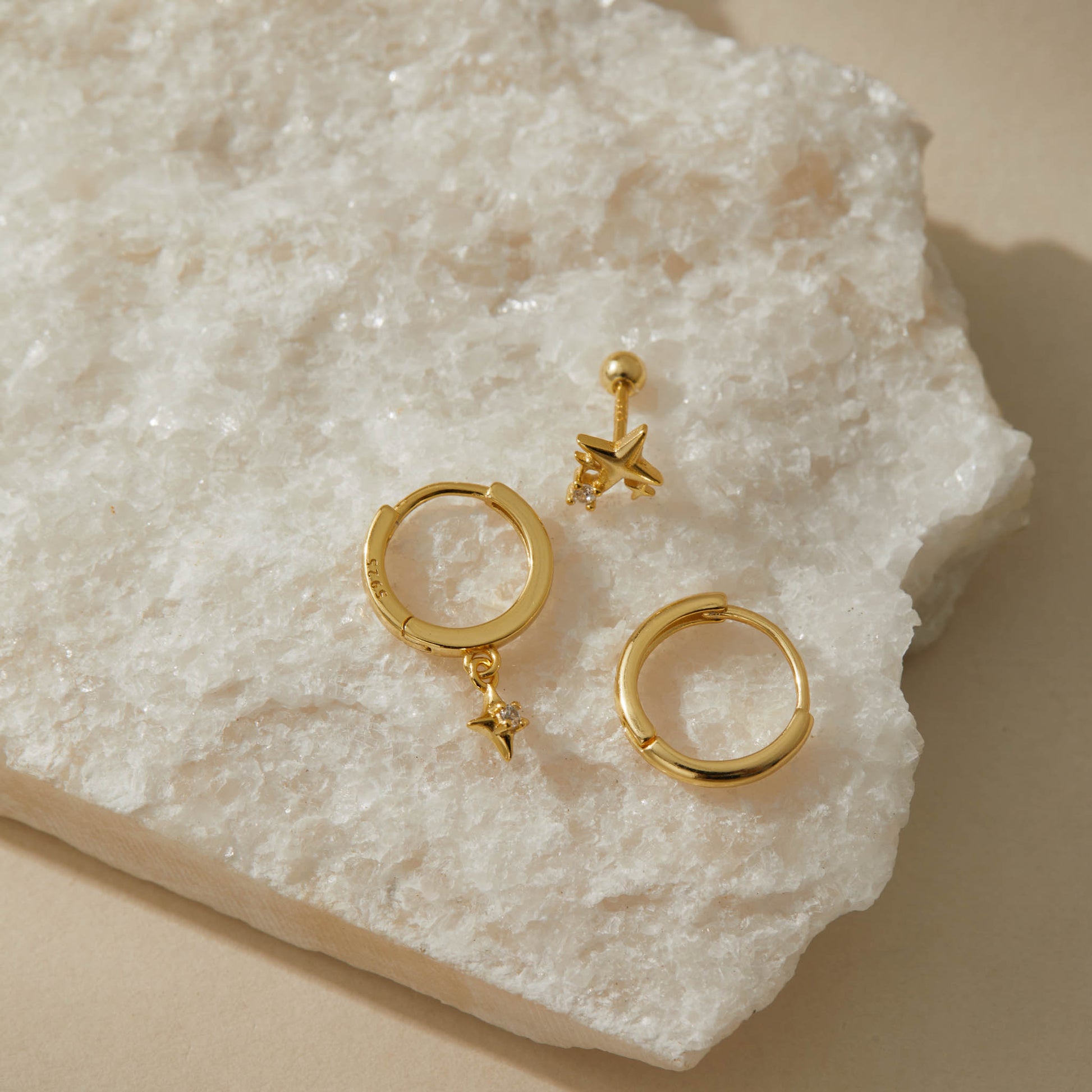 Overhead view of the gold star earring set on white quartz, 925 stamp visible on a huggie