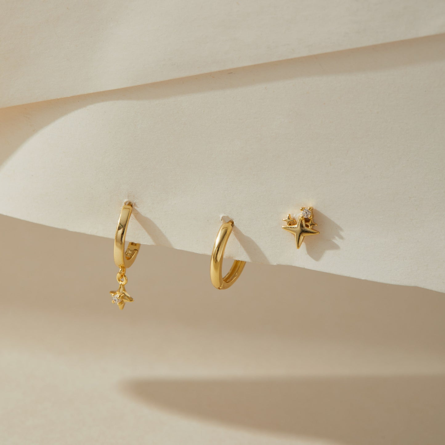 Gold plated star huggie earring set of three on cream paper, two hoops and a star stud