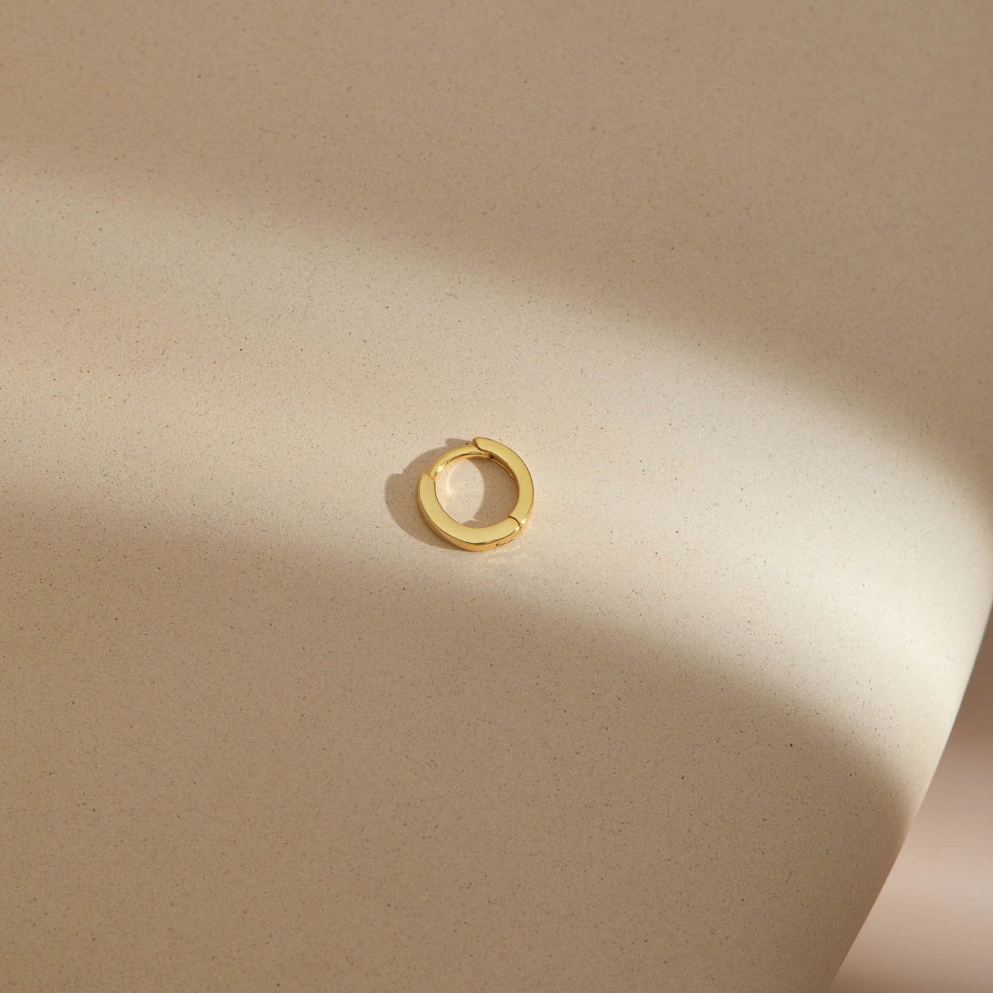 Plain gold plated huggie hoop earring with a smooth polished band and hinged snap closure