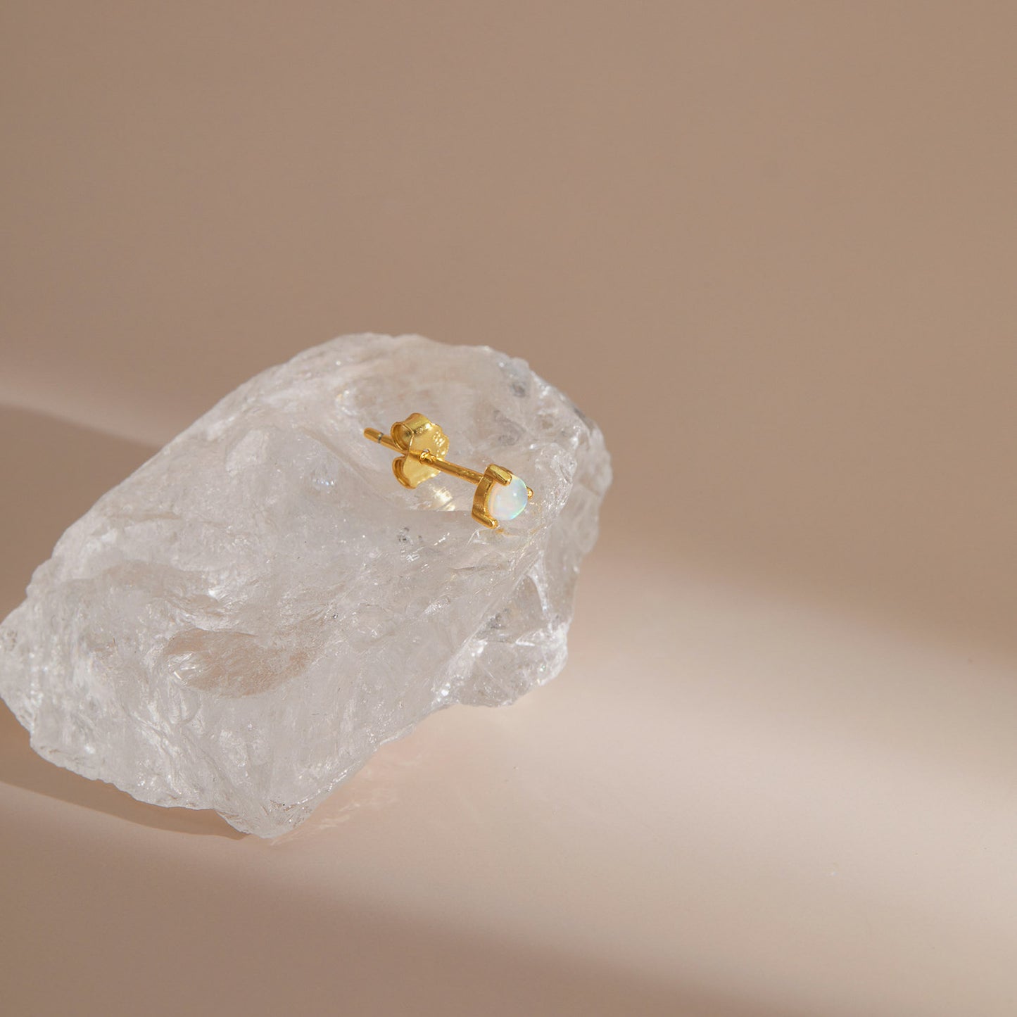 Gold plated opal stud earring with a single round opal in a claw setting, resting on raw quartz