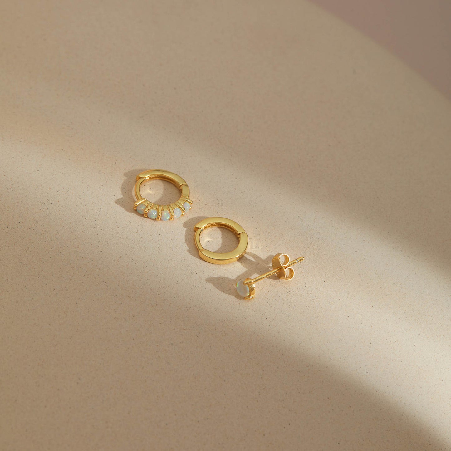 Gold plated opal earring set of three, opal huggie hoop, plain huggie hoop and opal stud on beige