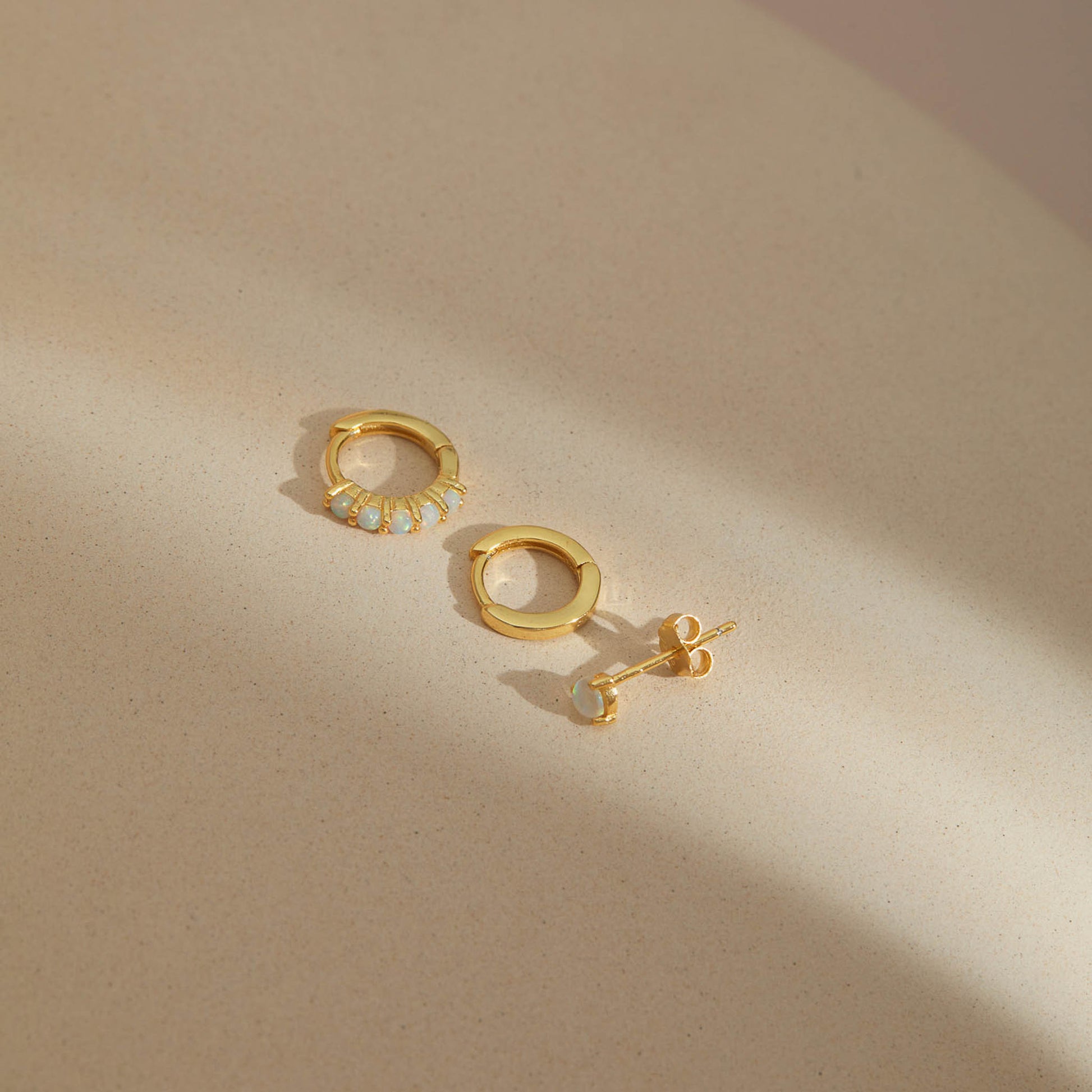 Gold plated opal earring set of three, opal huggie hoop, plain huggie hoop and opal stud on beige