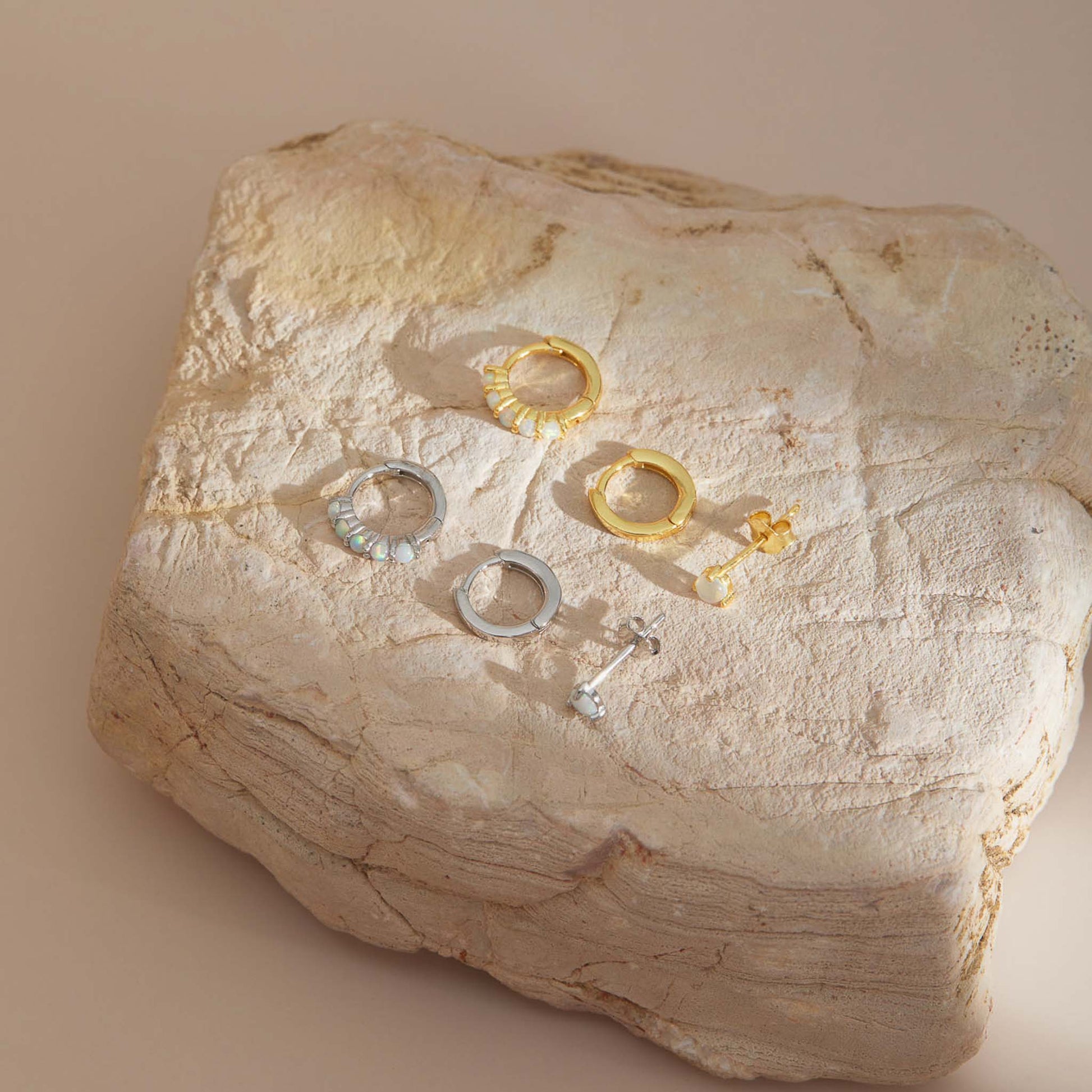 Gold plated and sterling silver opal earring sets of three shown together on a travertine slab