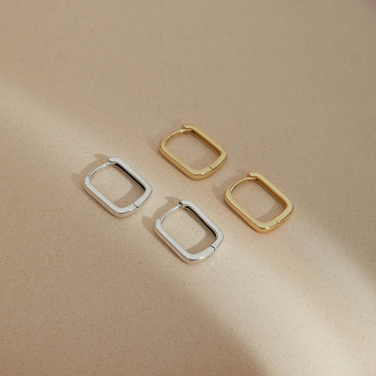 Minimalist rectangular huggie earrings in S925 sterling silver and gold plated displayed on a neutral surface, showcasing soft geometric design and refined craftsmanship.