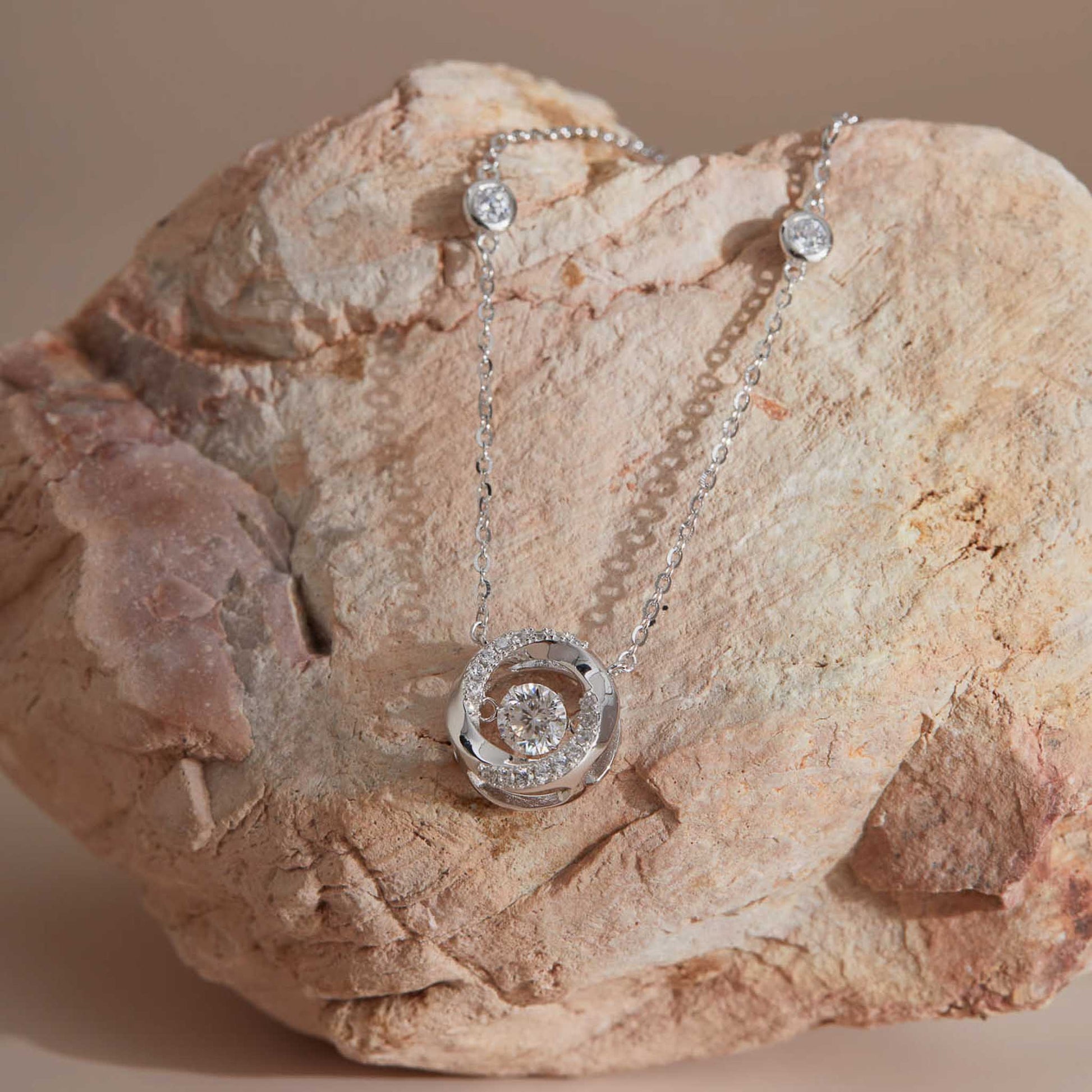 Sterling silver moissanite dancing stone spiral pendant on sandstone, station chain visible