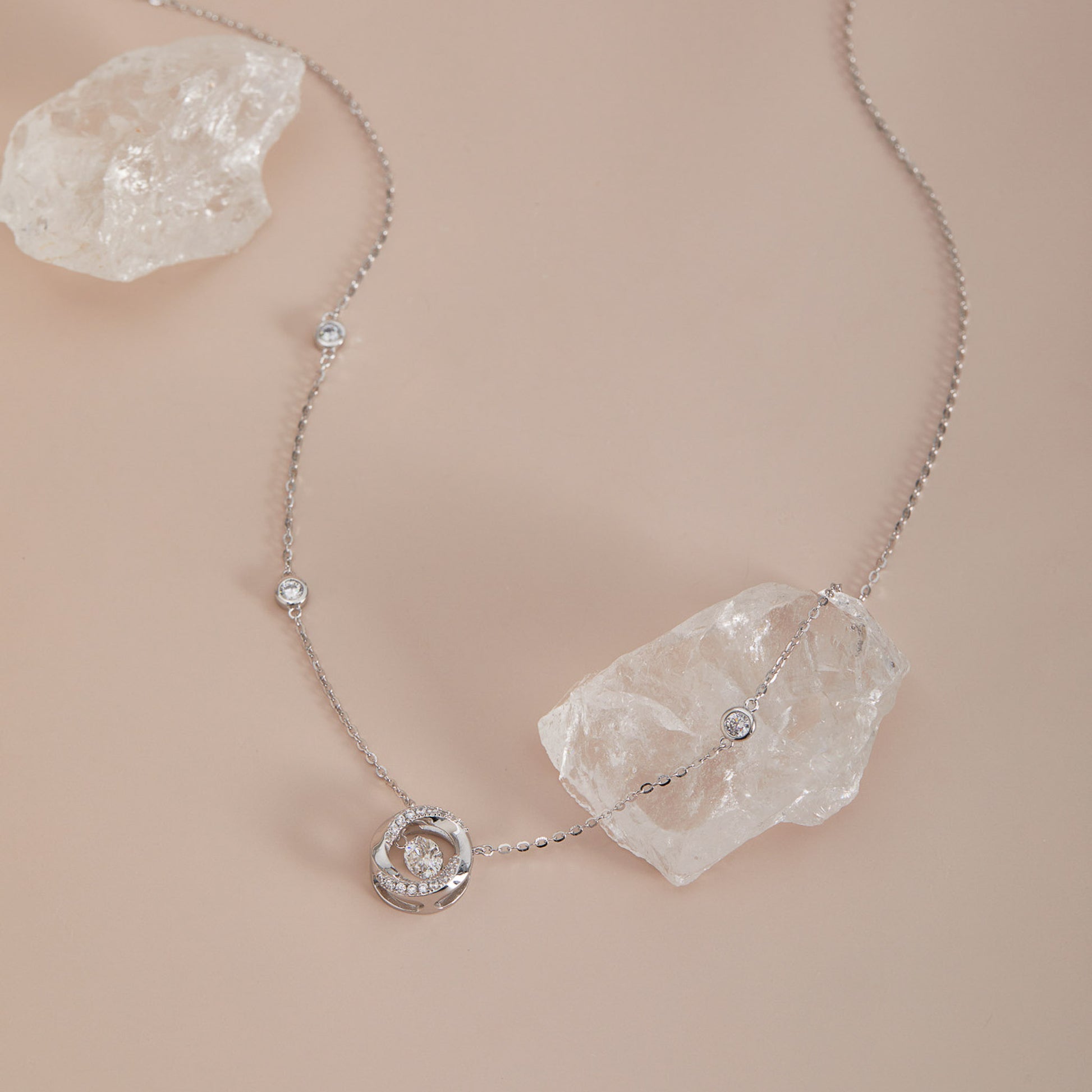 Sterling silver moissanite dancing stone necklace with station chain, draped over crystal quartz