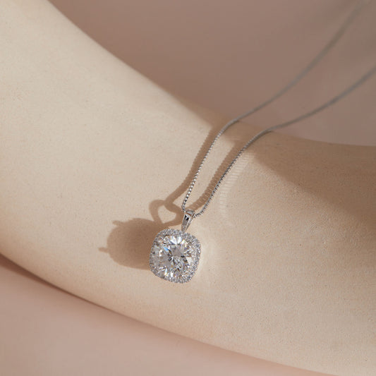 Sterling silver moissanite square halo pendant hanging against soft fabric, close-up