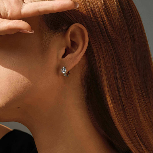 Woman wearing oxidized sterling silver sunflower huggie earring, close-up on ear