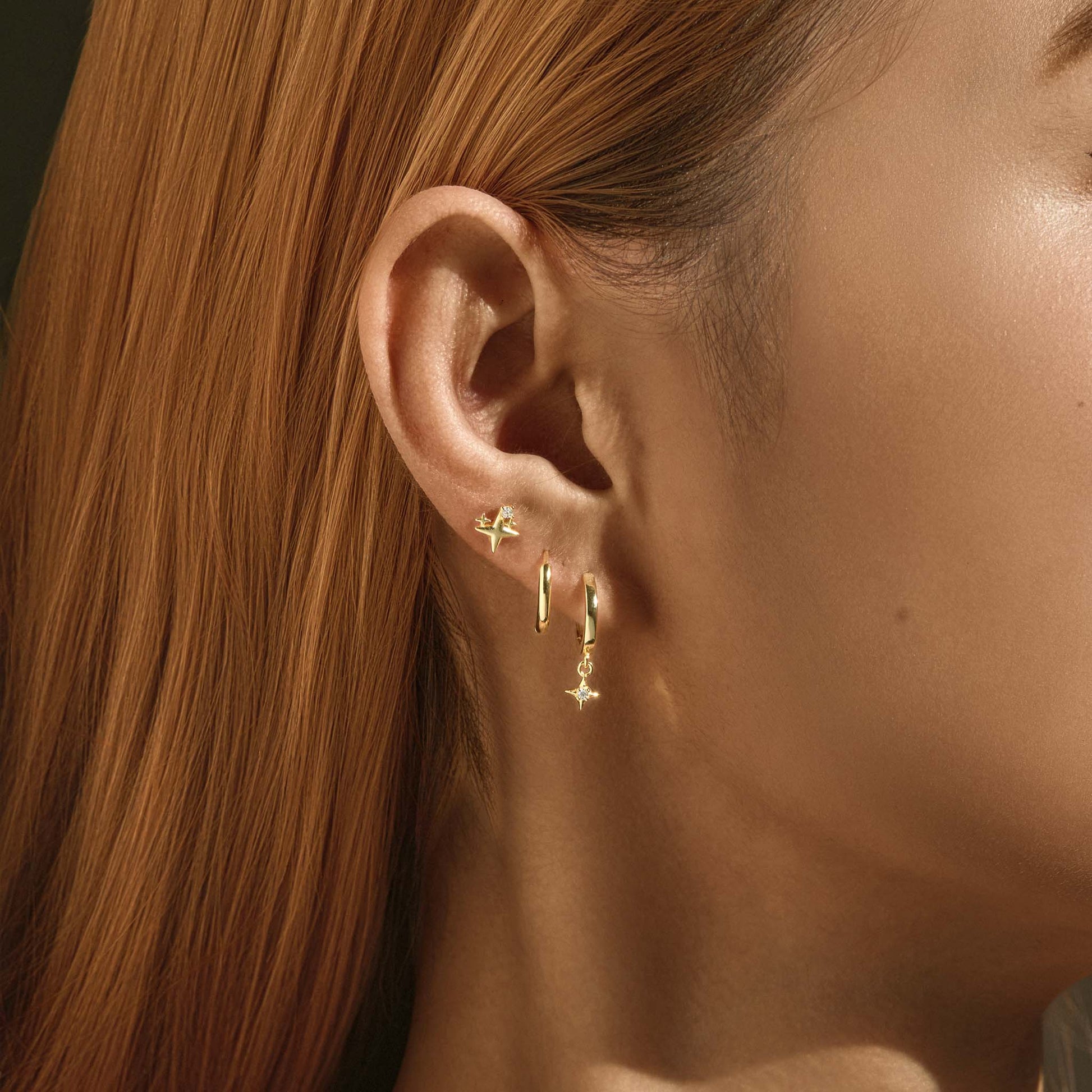 Model wearing the gold star huggie earring stack, star stud above two hoops on one ear