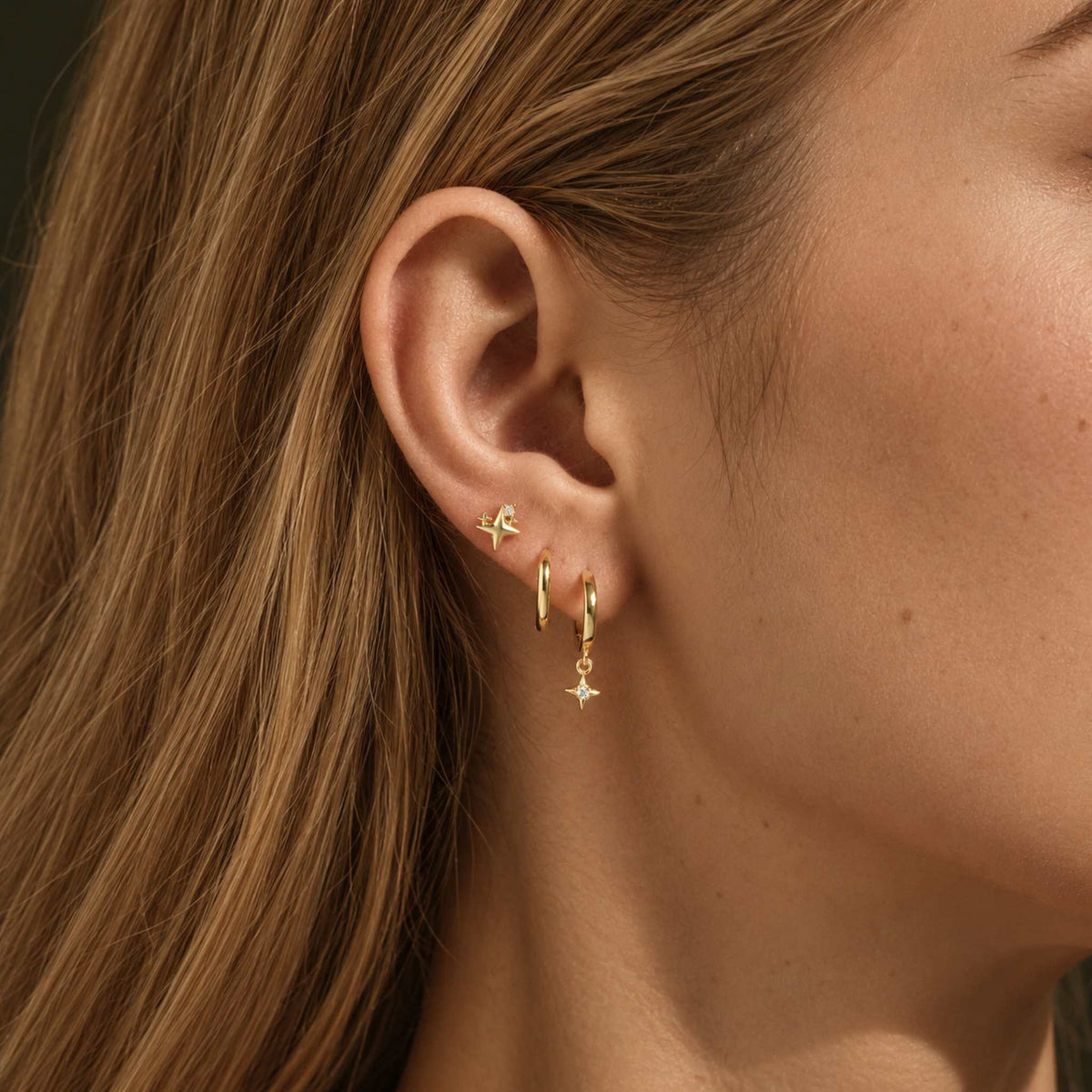 Model wearing the gold star huggie earring stack, star stud above two hoops on one ear