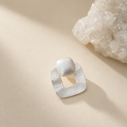 Brushed matte sterling silver stud earring with textured open-square frame and cushion top, on cream background