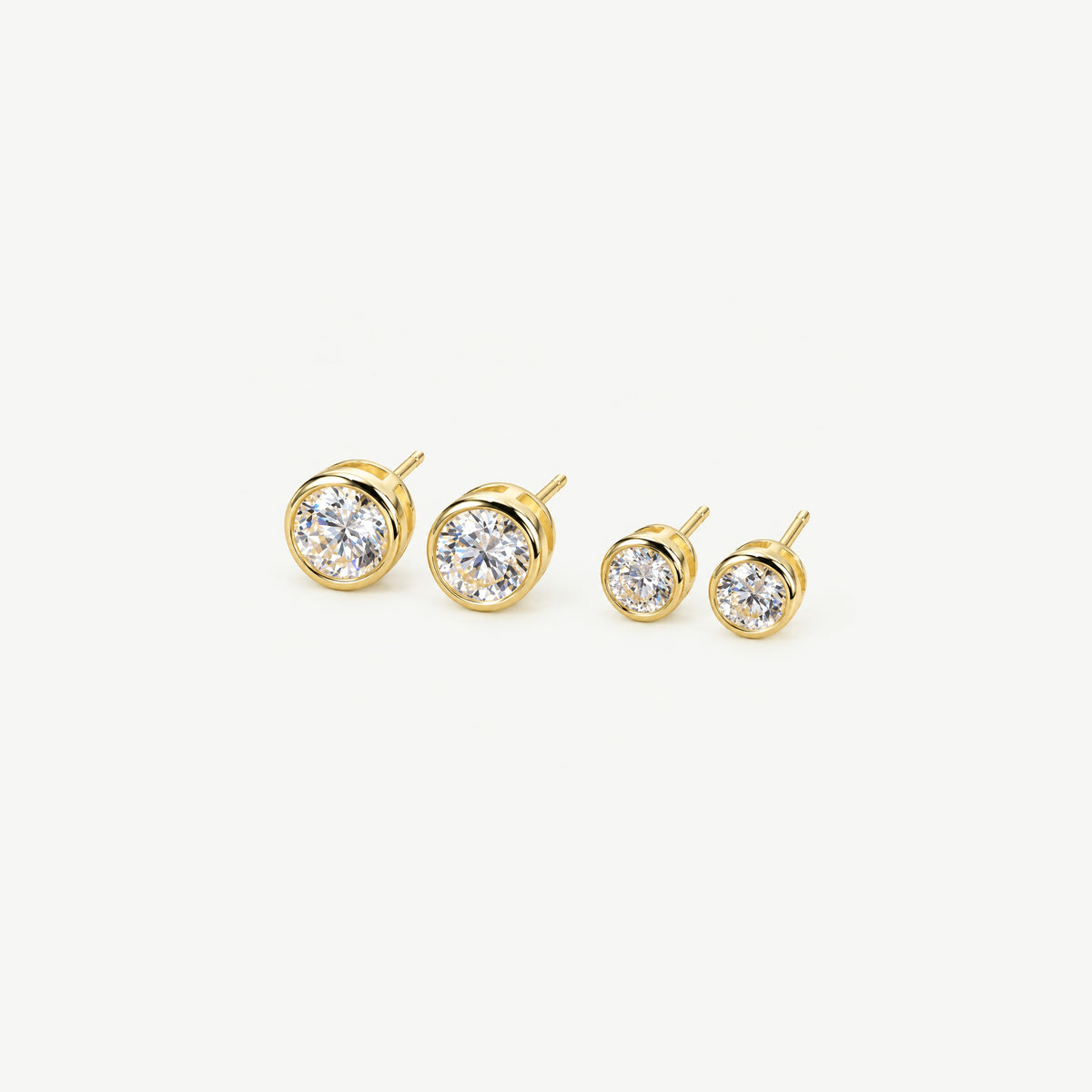 Two pairs of gold bezel moissanite stud earrings side by side, 1 ct pair on the left and 0.5 ct pair on the right