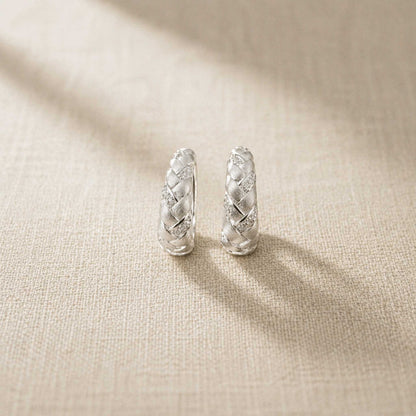 Pair of brushed sterling silver braided huggie hoop earrings with pavé accents, on linen with sunlight shadows