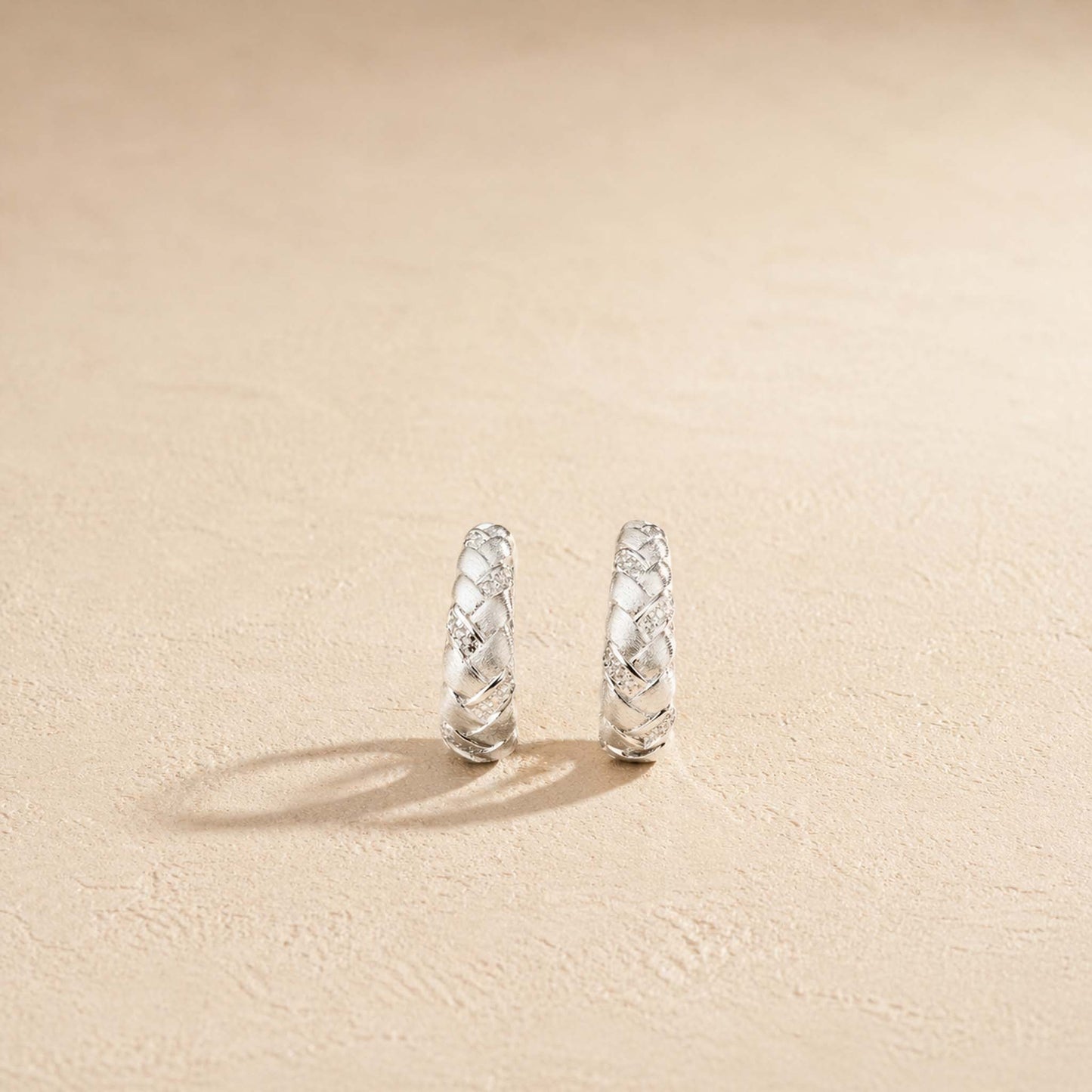 Brushed sterling silver braided huggie hoop earring with pavé accents, on cream background
