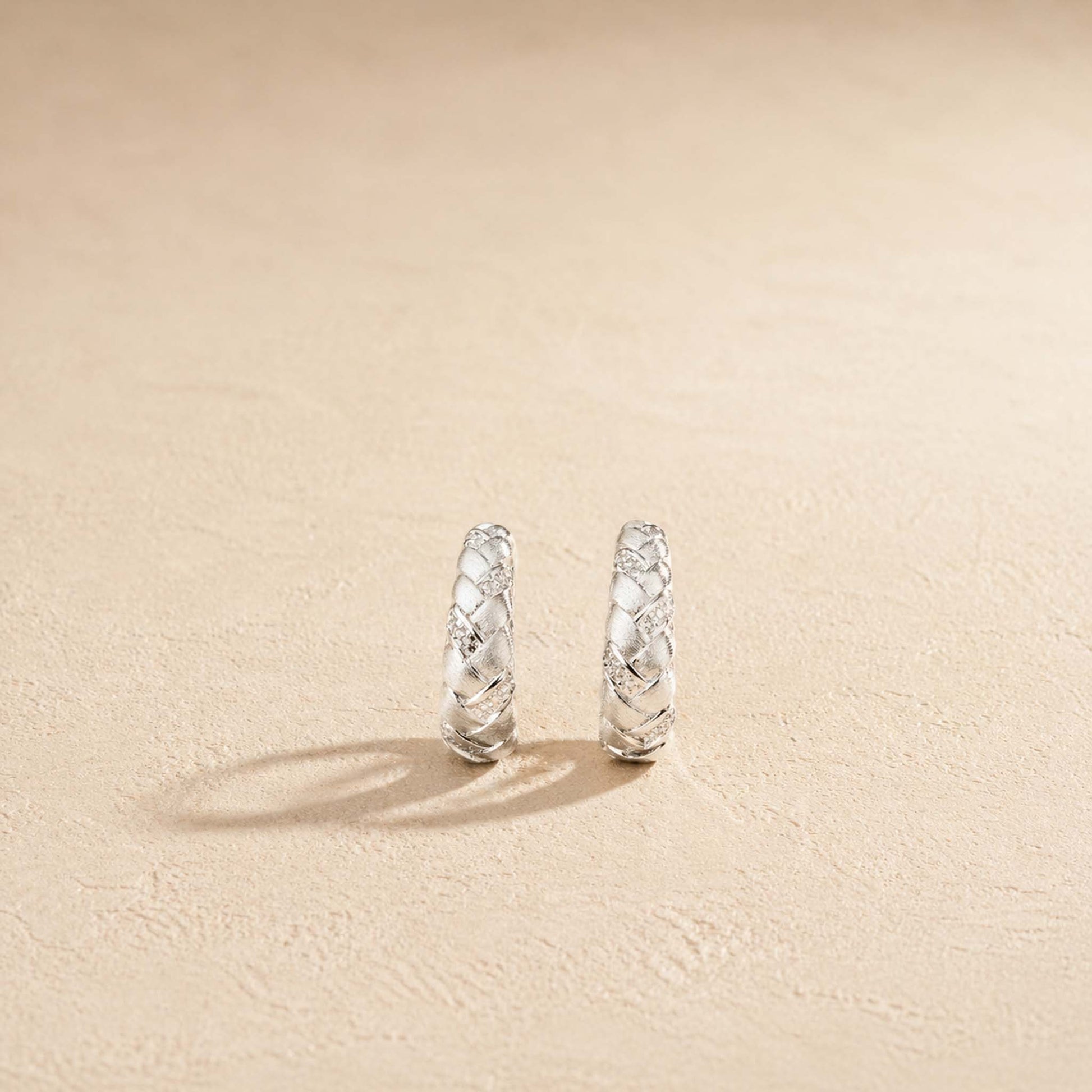Brushed sterling silver braided huggie hoop earring with pavé accents, on cream background