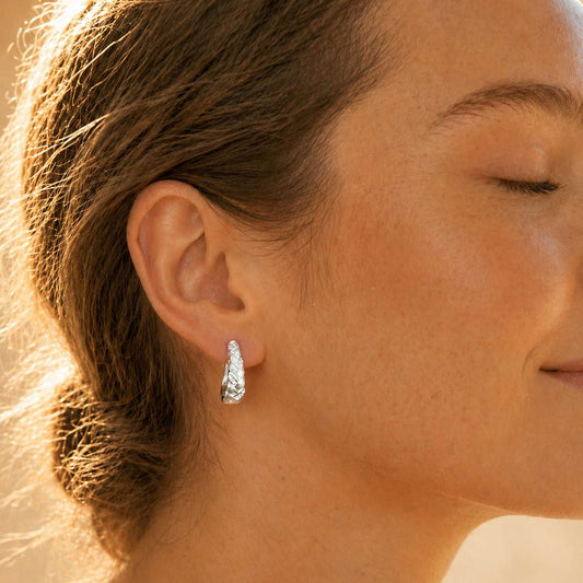 Woman wearing brushed sterling silver braided huggie hoop earring, side profile in warm sunlight