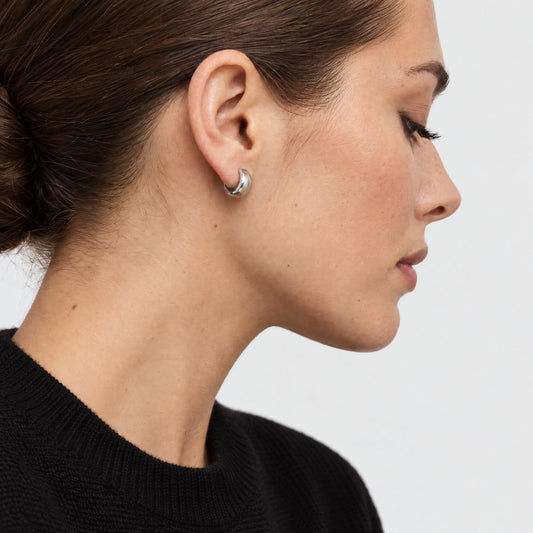 Side profile of a woman in a black knit sweater wearing a chunky white gold-plated sterling silver huggie earring