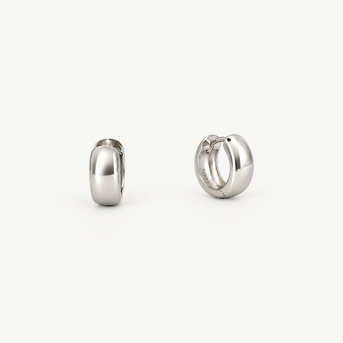 Pair of chunky round huggie hoop earrings in white gold-plated sterling silver, one face-on, one turned to show inside