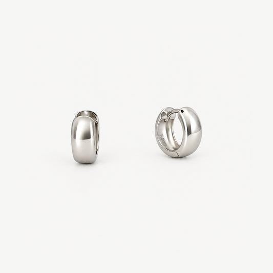 Pair of chunky round huggie hoop earrings in white gold-plated sterling silver, one face-on, one turned to show inside