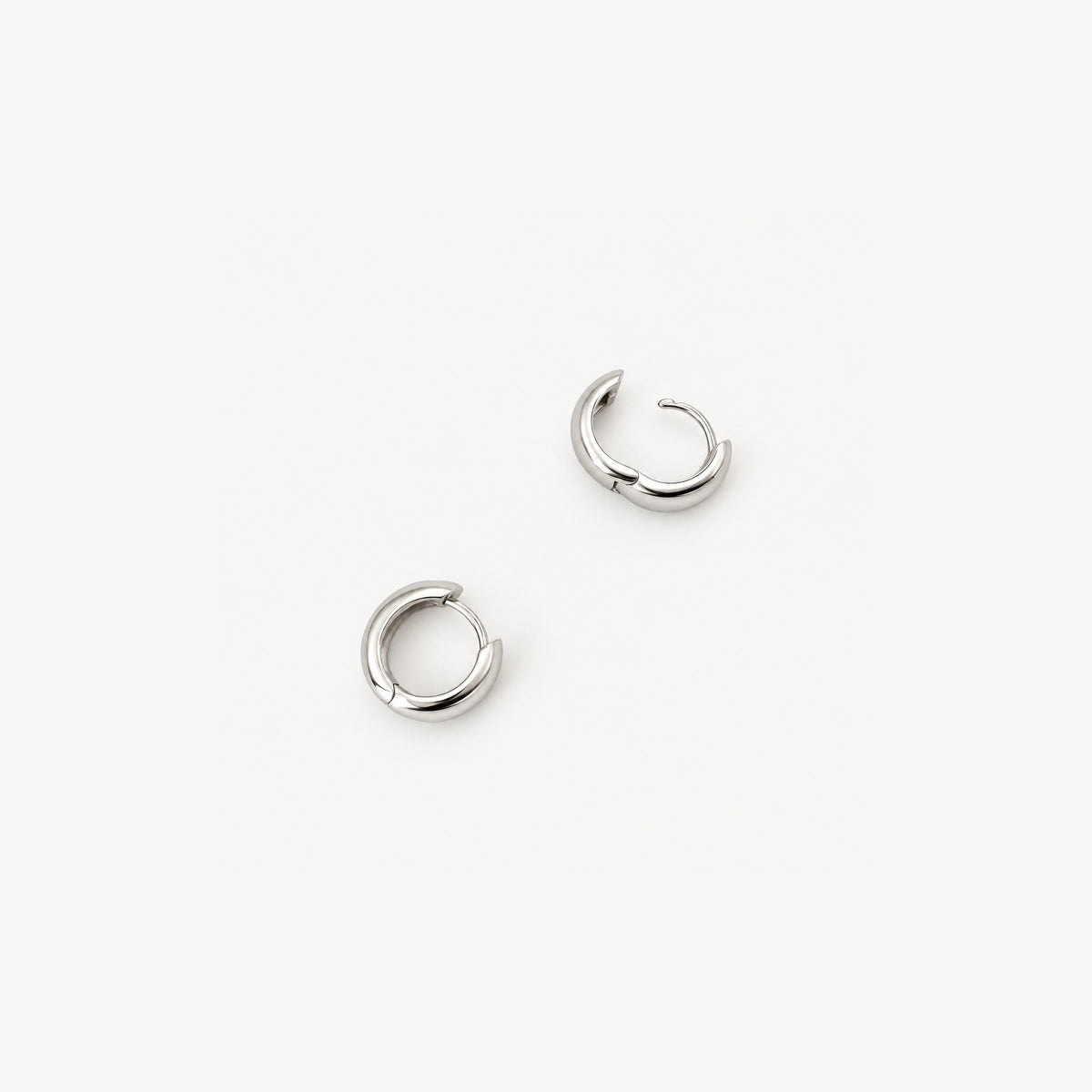 Two chunky dome huggie earrings from above, one open on its hinge to show the clicker wire and the polished inner band
