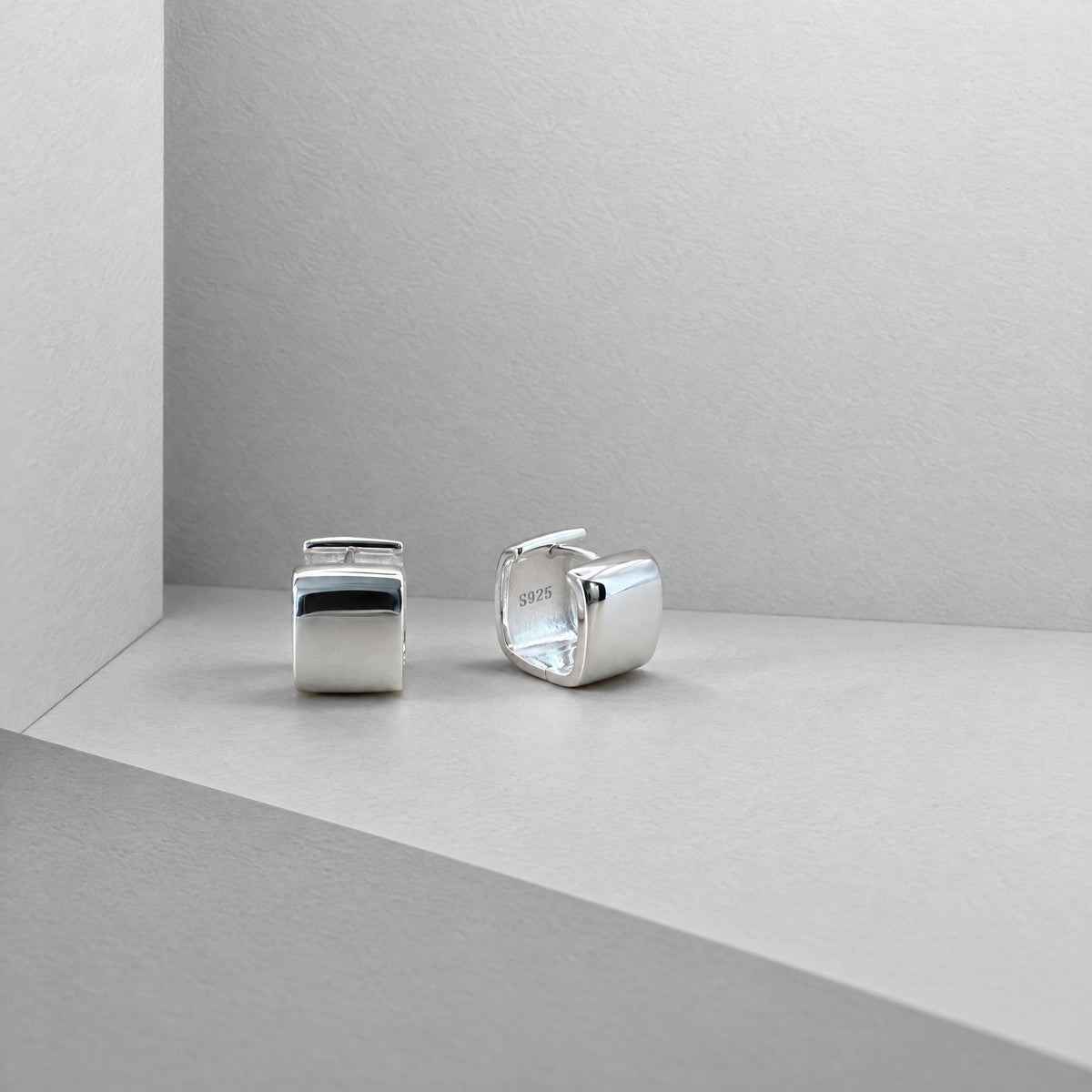 Pair of chunky square sterling silver huggies in a grey card corner, polished front and square opening shown