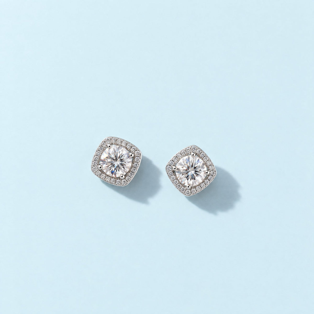 Colorless moissanite halo stud earrings in sterling silver lying face up on a pale ice blue backdrop