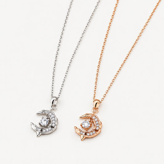 Two crescent moon dolphin necklaces, one 18k gold-plated and one sterling silver, pendants side by side on off-white