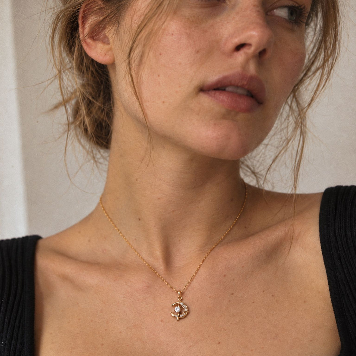 Woman in a black ribbed top wearing an 18k gold-plated crescent moon dolphin necklace just below the collarbone