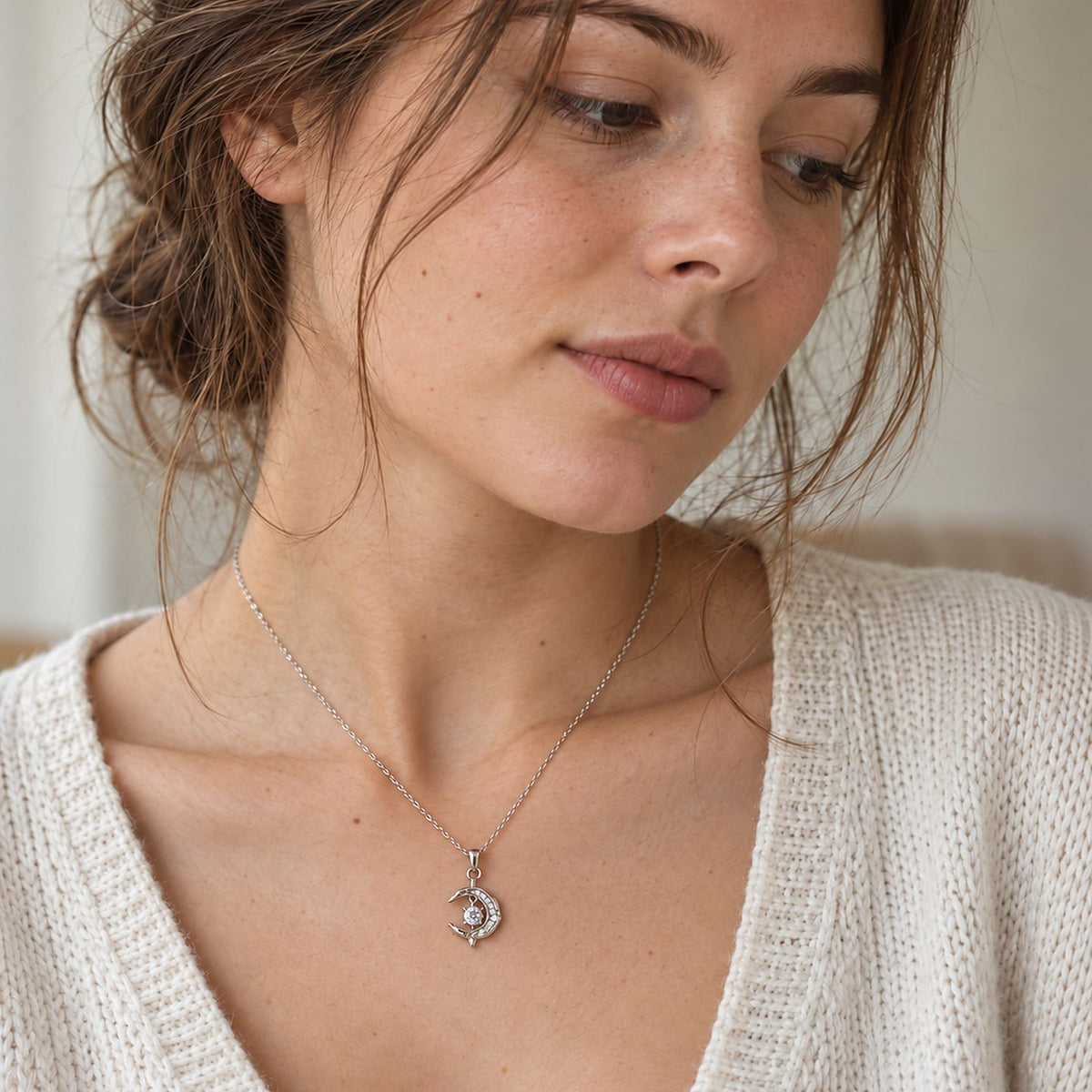Woman with loose brown hair looking down in a knit sweater, a sterling silver crescent moon dolphin pendant at her neck