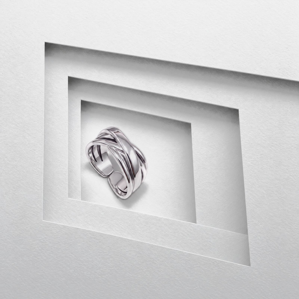 Sterling silver crossover ring standing in a stepped grey card opening, polished bands crossing over the open band