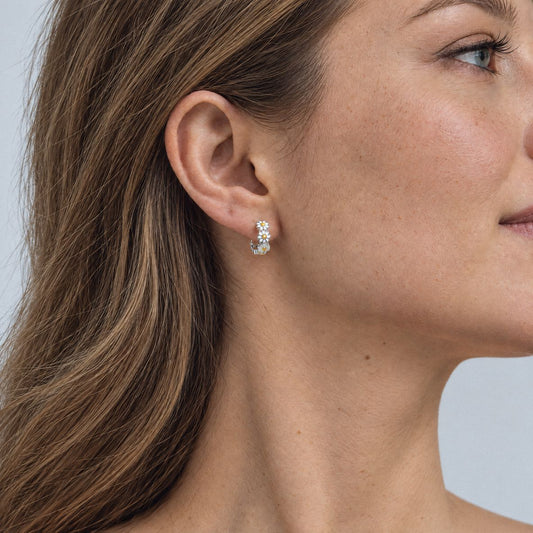 Woman with light brown hair wearing a sterling silver daisy huggie earring, side profile on a light grey backdrop