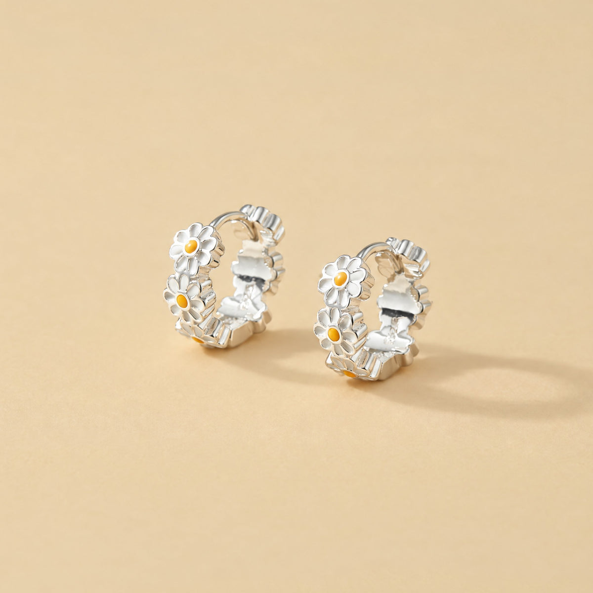 Pair of sterling silver daisy huggie earrings standing upright on pale yellow, white enamel petals to the front
