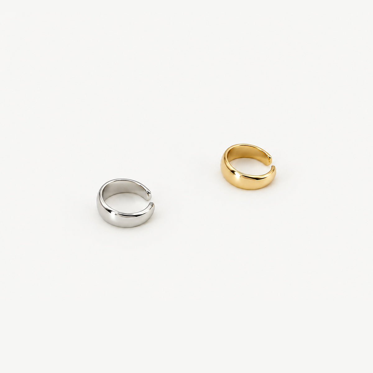 Two dome ear cuffs side by side, one in sterling silver and one gold-plated, polished open bands