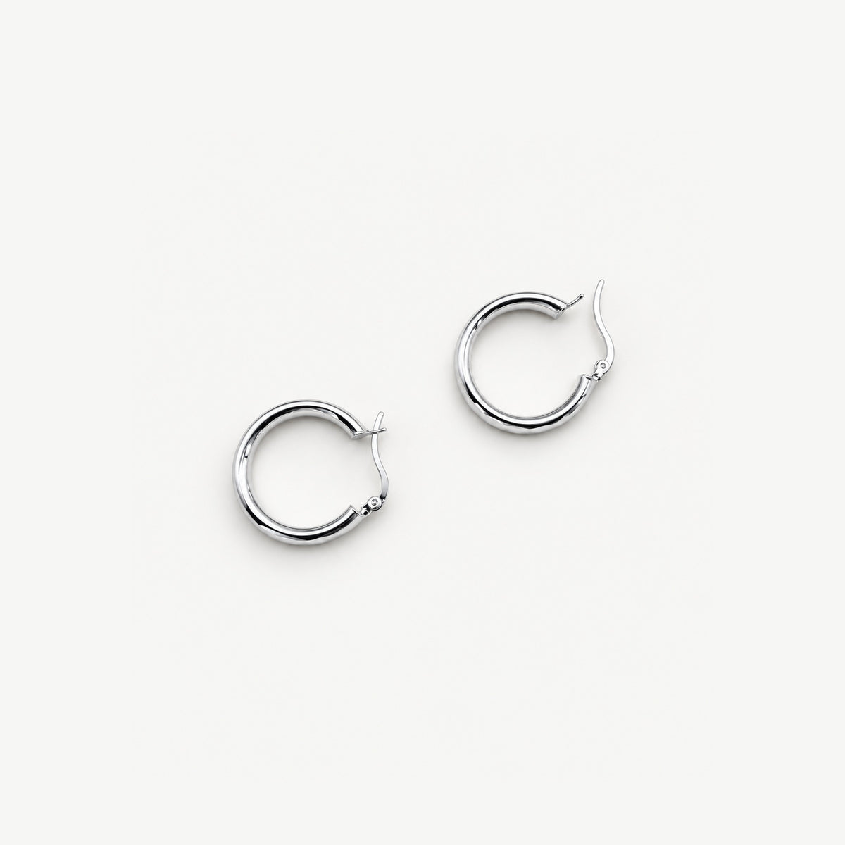 Two faceted sterling silver hoop earrings lying flat with the click closures open, seen from above on white