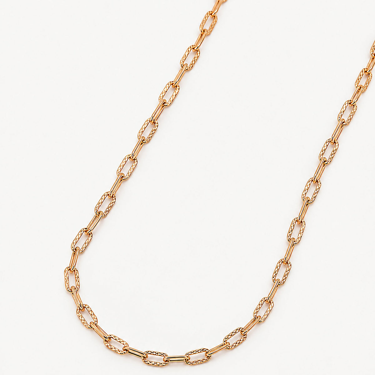 Close view of the gold paperclip chain, long smooth links alternating with short faceted links that catch the light